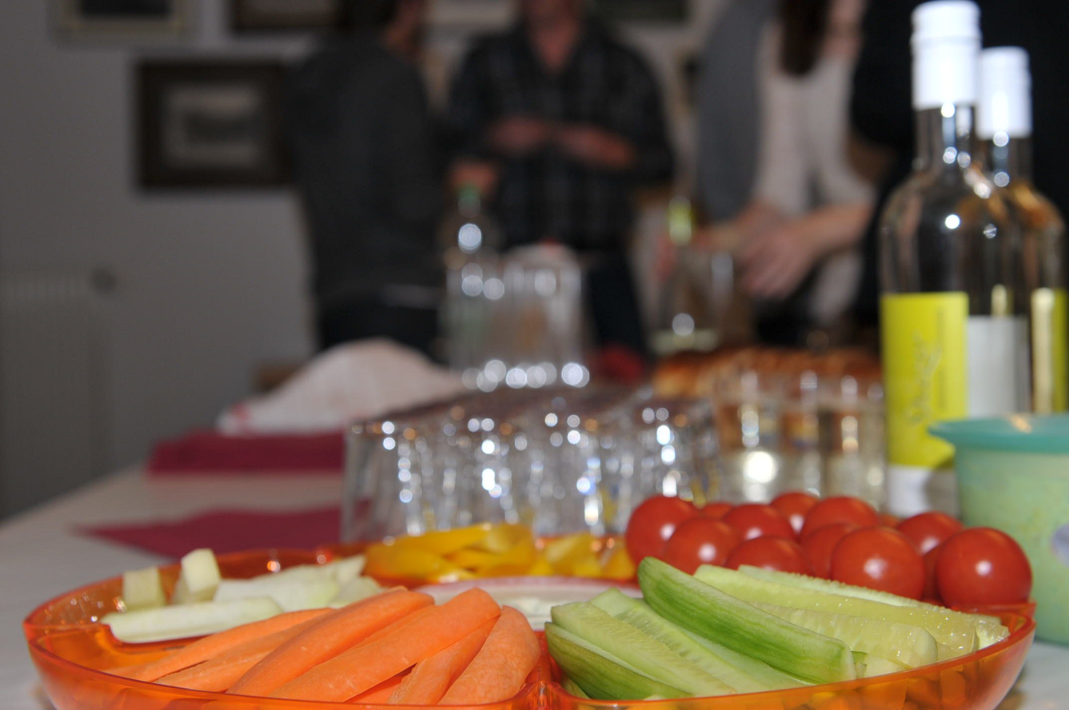 Gemüse zum Dippen auf Tisch. Im Hintergrund verschlossene Weissweinflaschen.