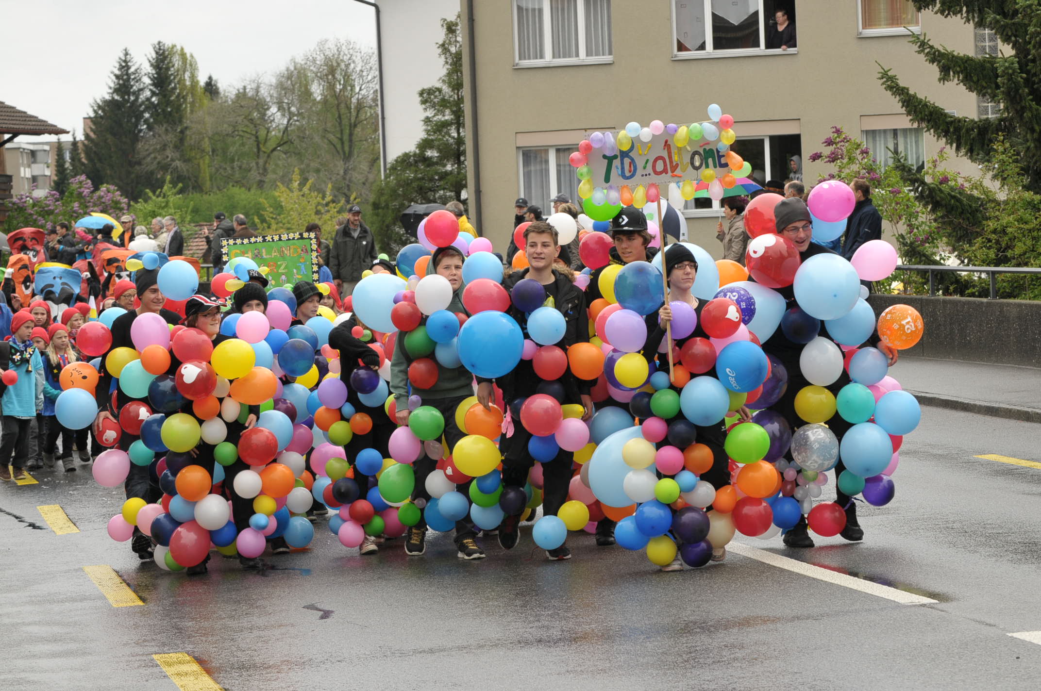 Schulkinder, welche sich in unzählige aufgeblasene Luftballone gehüllt haben.
