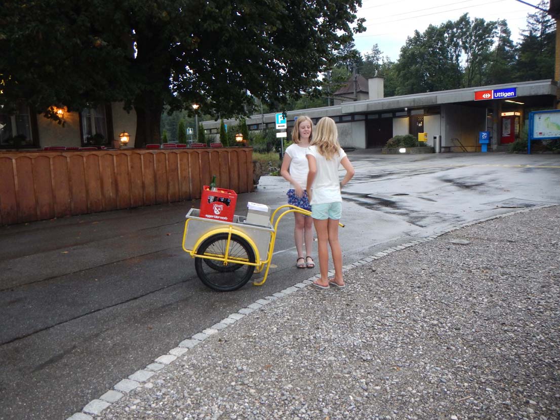 Zwei Mädchen mit Fahrradanhänger, in welchem sich unsere Getränke befinden, beim verregneten Bahnhof in Uttigen.