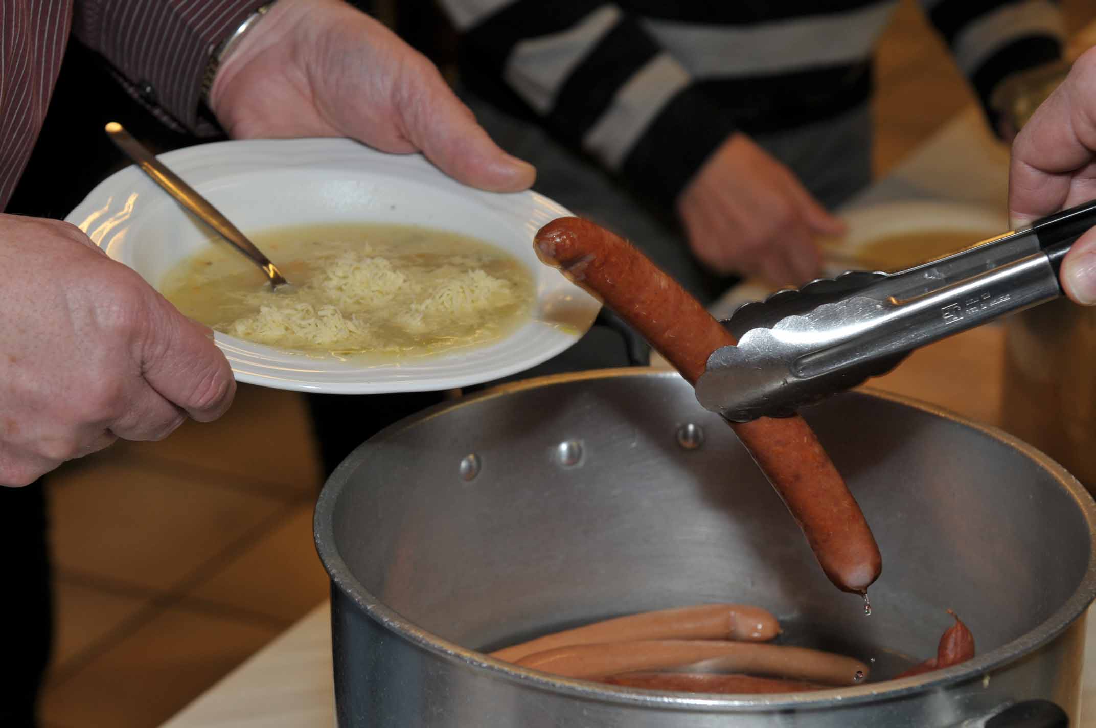 Wurst wird aus Pfanne genommen und auf Teller mit Suppe gelegt.