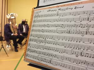 Noten "Happy Marching Band" auf Notenständer. In der Ferne ein Bass.