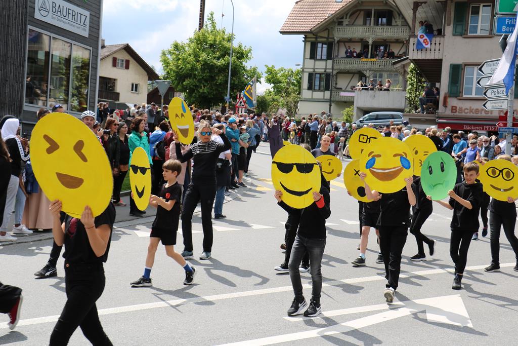 Schwarz gekleidete Schulkinder mit überdimensionalen Smileys vor dem Kopf.